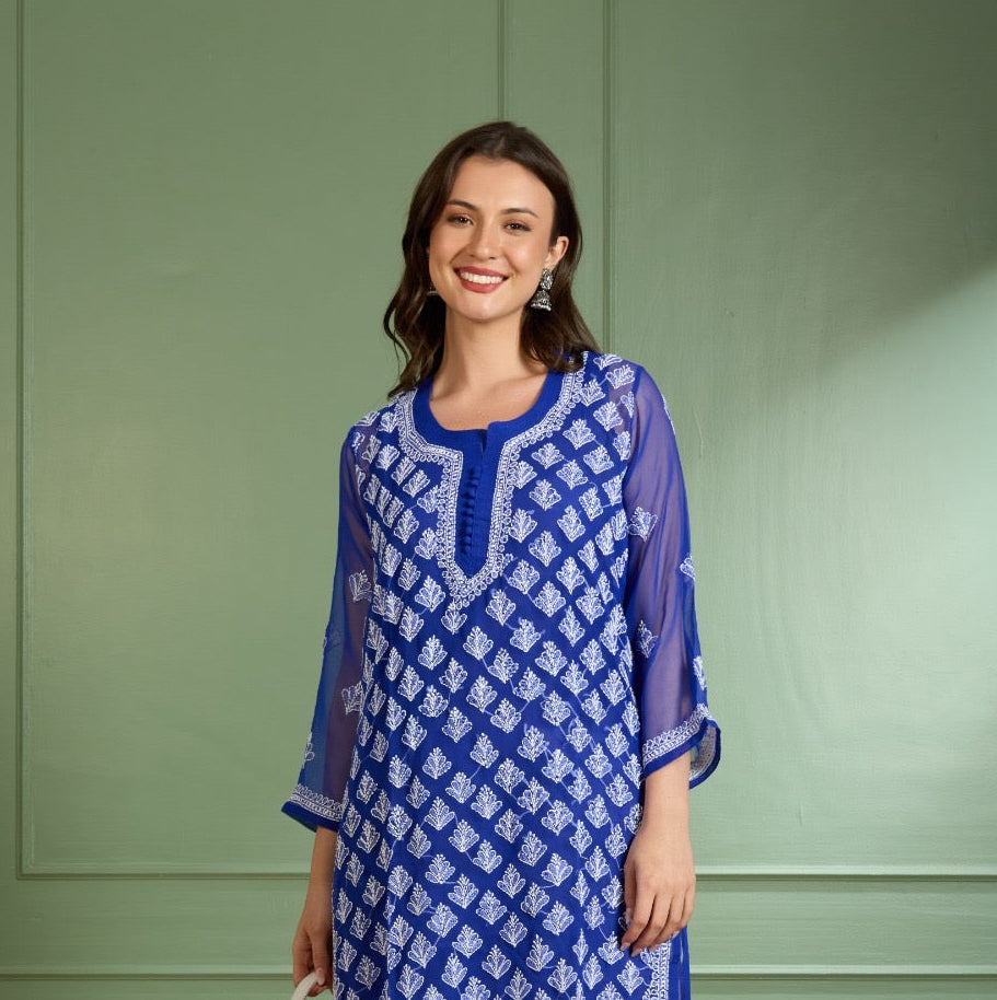 Woman wearing a blue and white patterned kurta with white pants against a green wall.